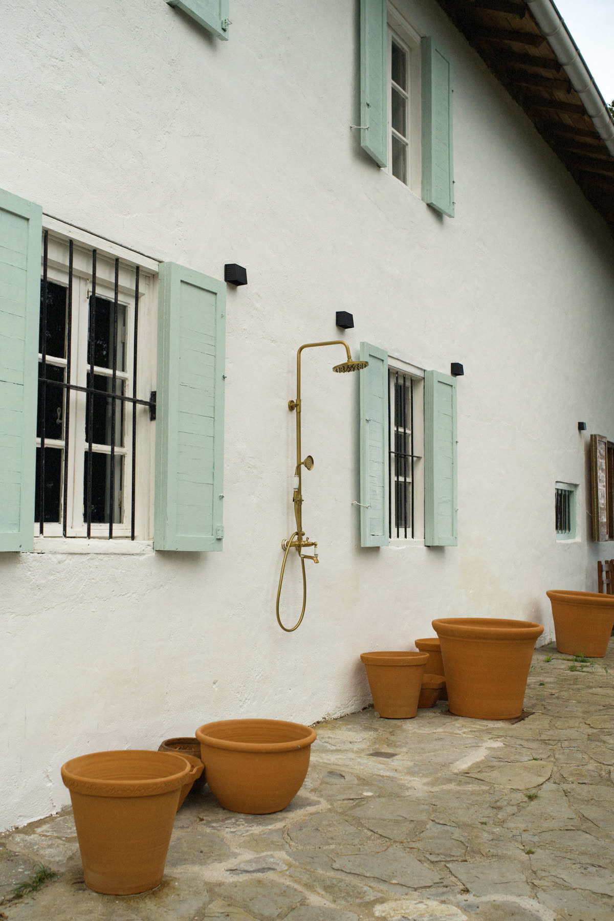 Ducha exterior de latón sobre la fachada encalada y contras verdes